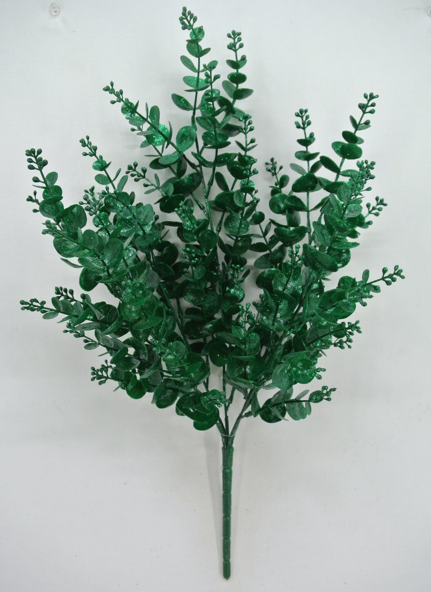 A bunch of green artificial leaves or branches, resembling a plant or a decorative element, is displayed against a white background.