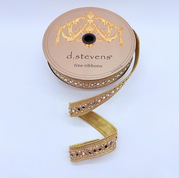 A spool of fine gold ribbon with a decorative pattern, placed on a white background.