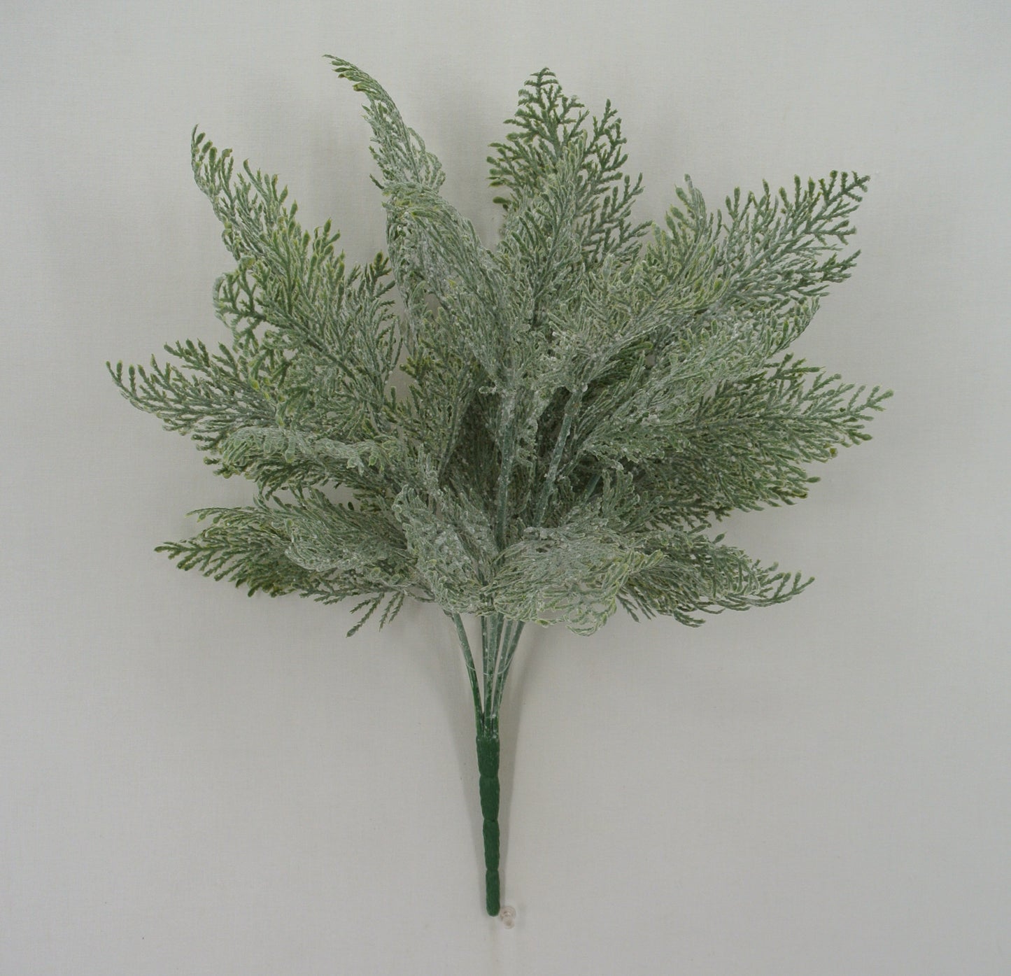 A bunch of green artificial fern-like leaves or branches against a plain white background.