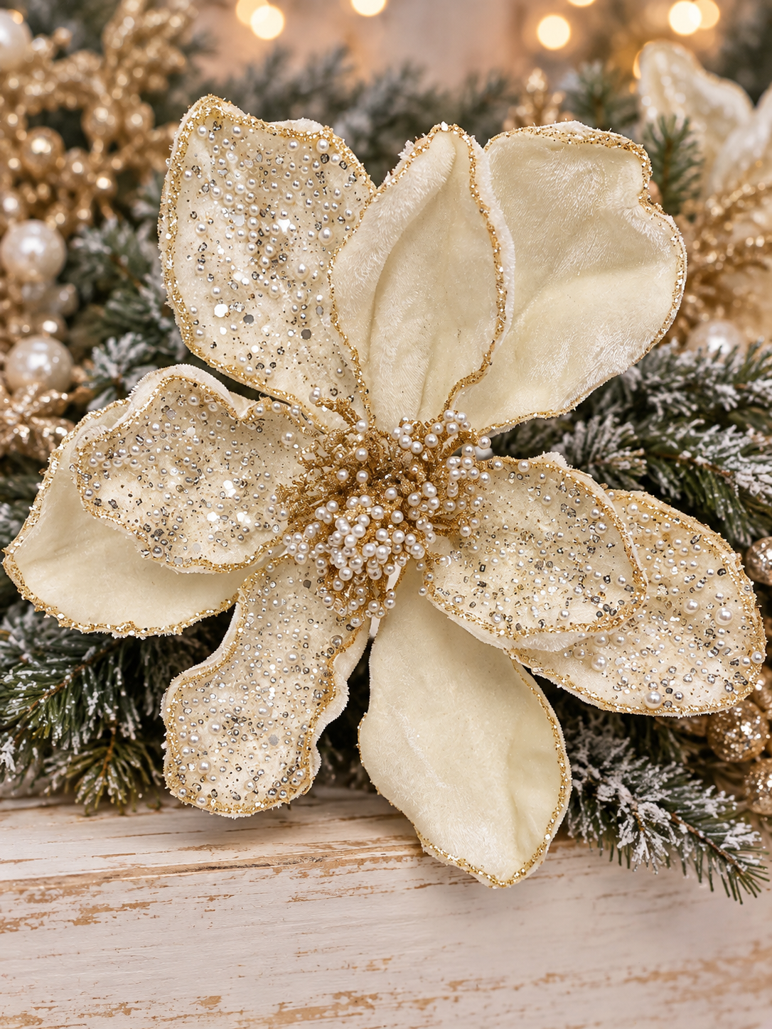A close-up of a large, ornate gold and white flower with sparkling embellishments, surrounded by greenery and twinkling lights.