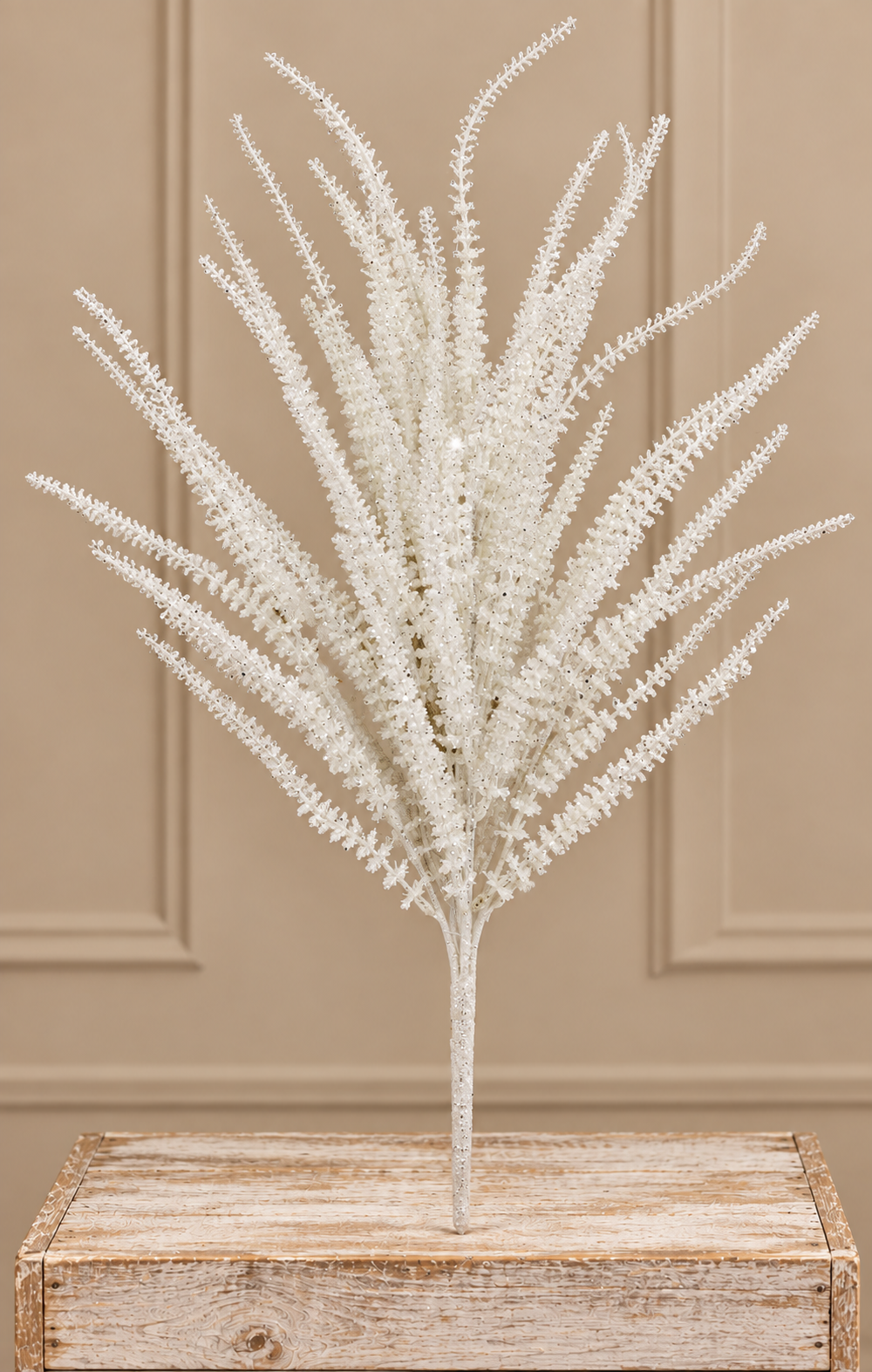 A bouquet of delicate white flowers is displayed on a wooden surface against a beige wall.