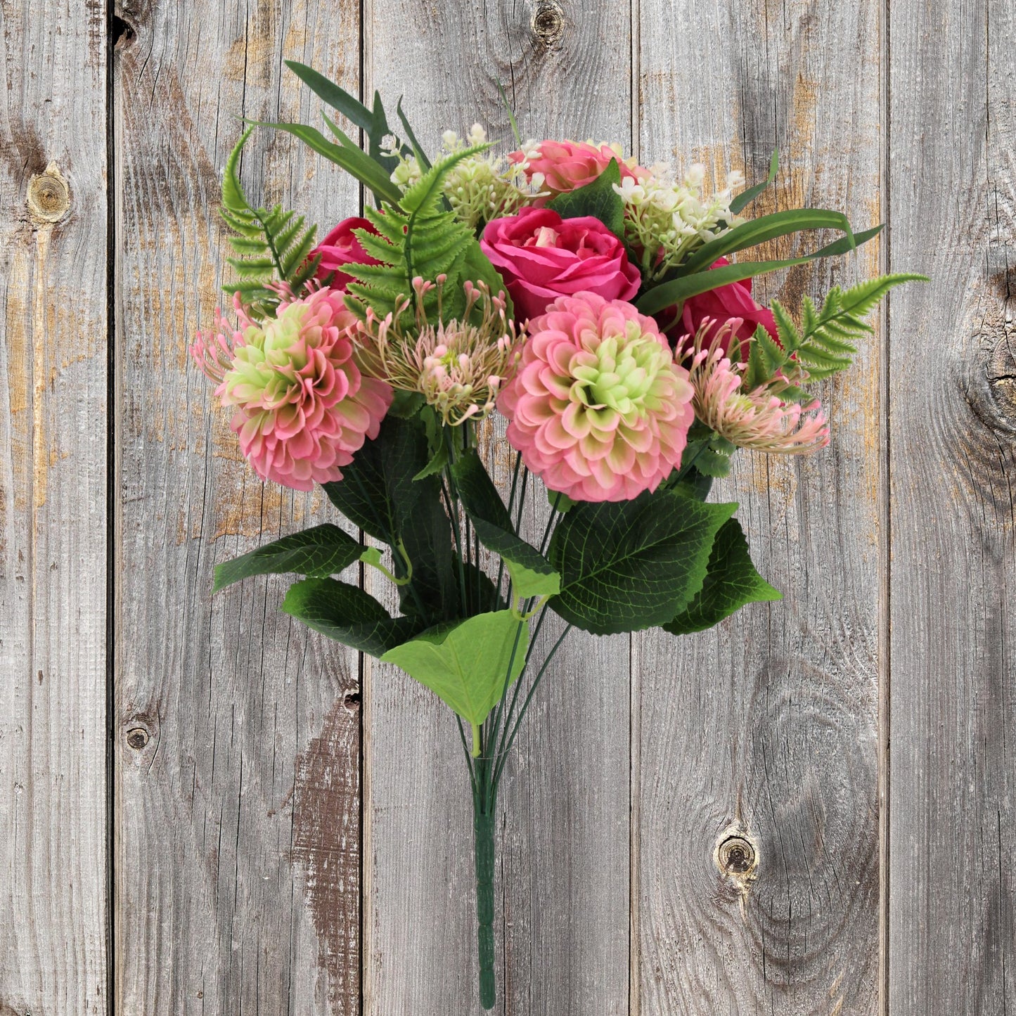 A bouquet of pink and green flowers, including roses and ferns, is displayed against a weathered wooden background.