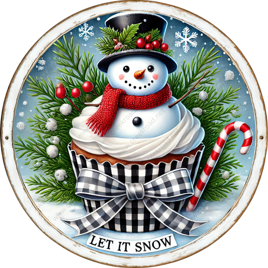 A snowman wearing a top hat and scarf sits atop a cupcake, surrounded by pine branches, berries, and a candy cane, with the phrase "Let it snow" displayed below.