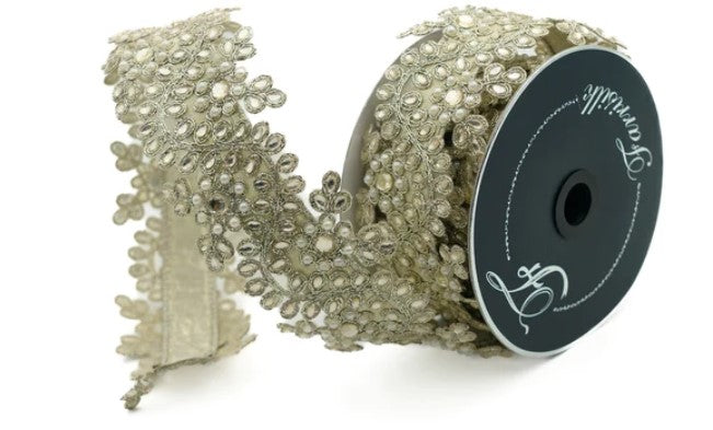 A spool of gold-colored lace ribbon with a floral pattern, lying on a white background.