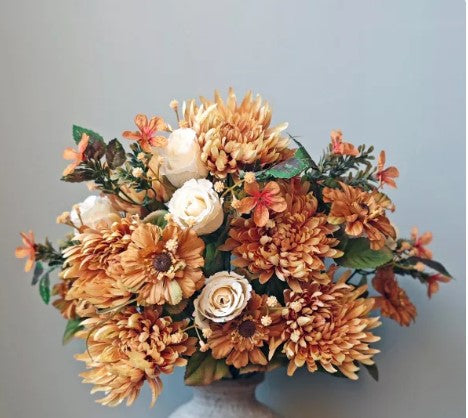 A bouquet of vibrant orange and white flowers, including chrysanthemums, roses, and daisies, arranged in a vase against a light blue background.