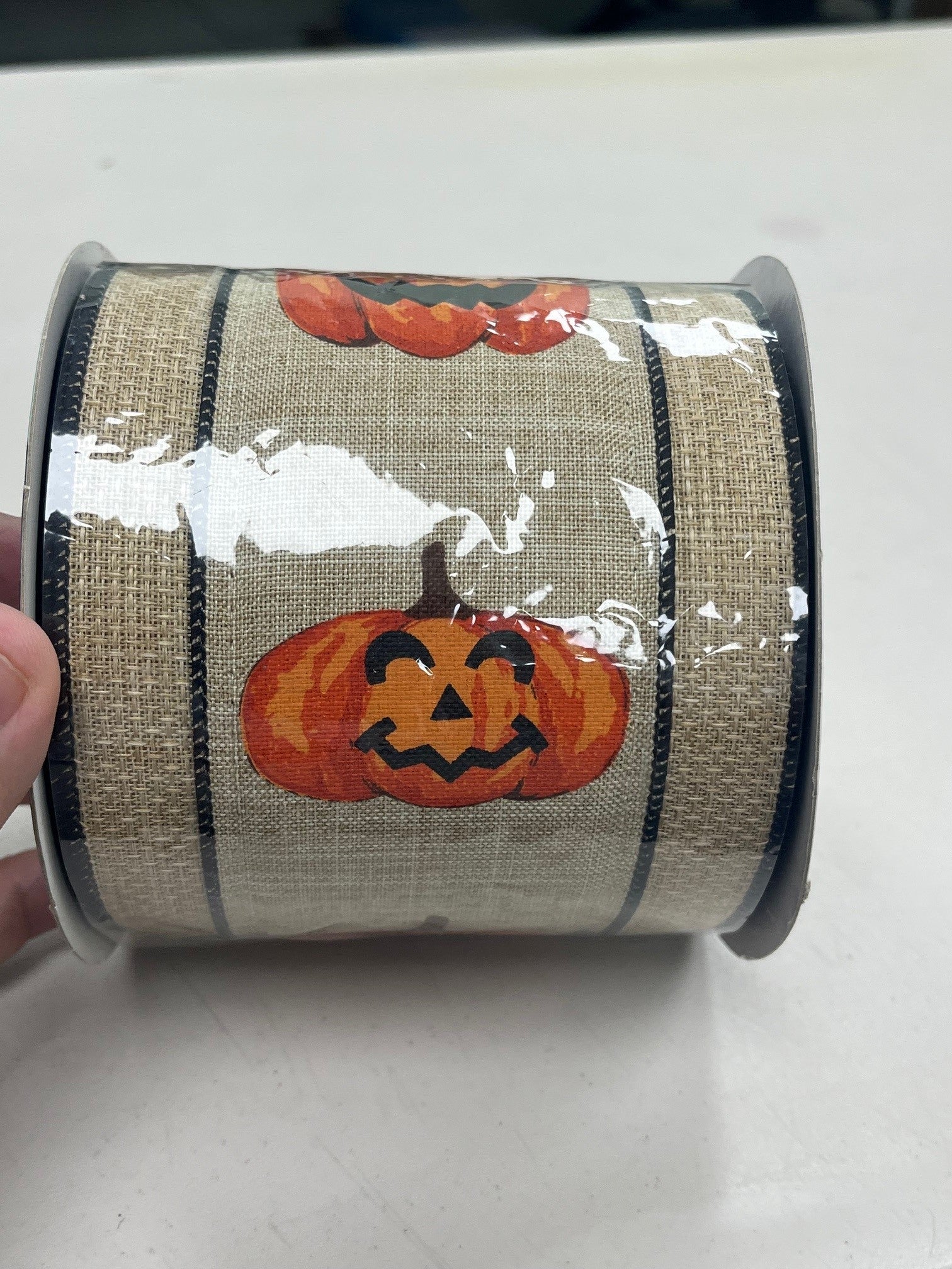 A hand is holding a roll of burlap ribbon with a pumpkin design on it.