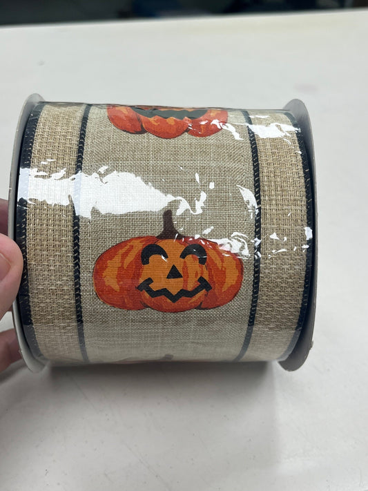 A hand is holding a roll of burlap ribbon with a pumpkin design on it.