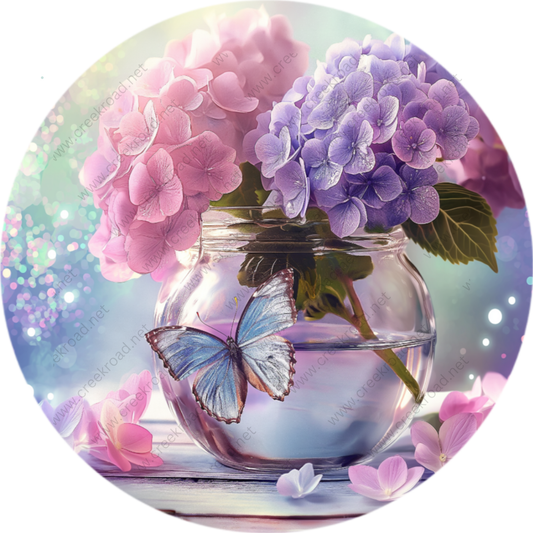 A glass vase filled with purple hydrangeas and pink hydrangeas, with a blue butterfly resting on the water's surface.