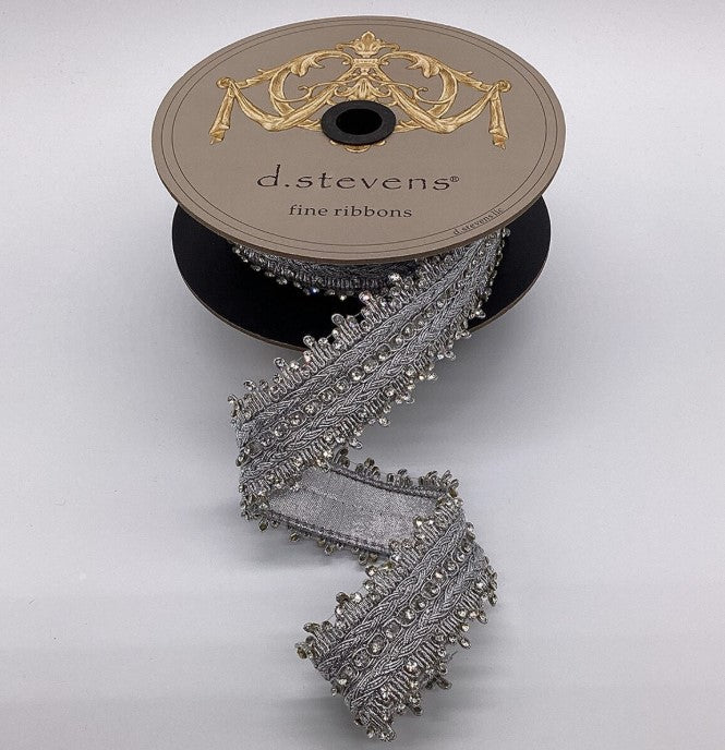 A spool of silver ribbon with a decorative trim, placed on a plain background.