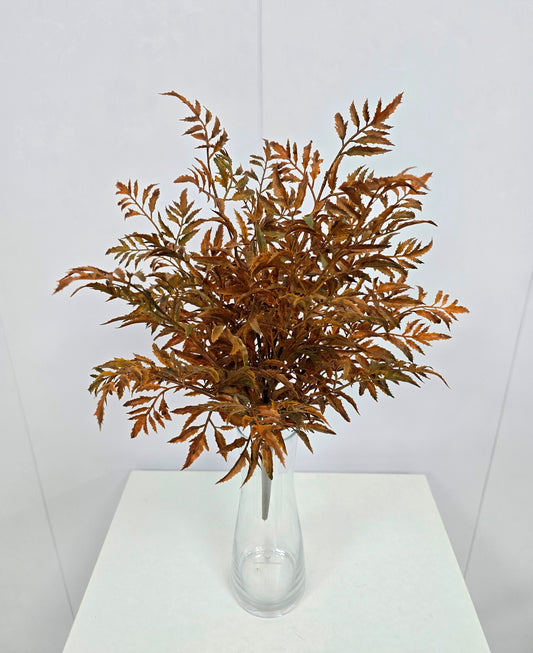 A bouquet of brown leaves in a clear glass vase, placed on a white surface against a plain background.