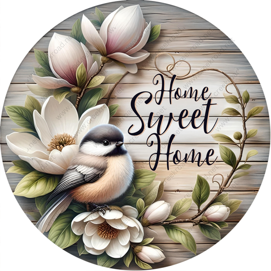 A round wooden sign with a bird perched on a branch, surrounded by white flowers and greenery. The sign has the text "Home Sweet Home" written on it.