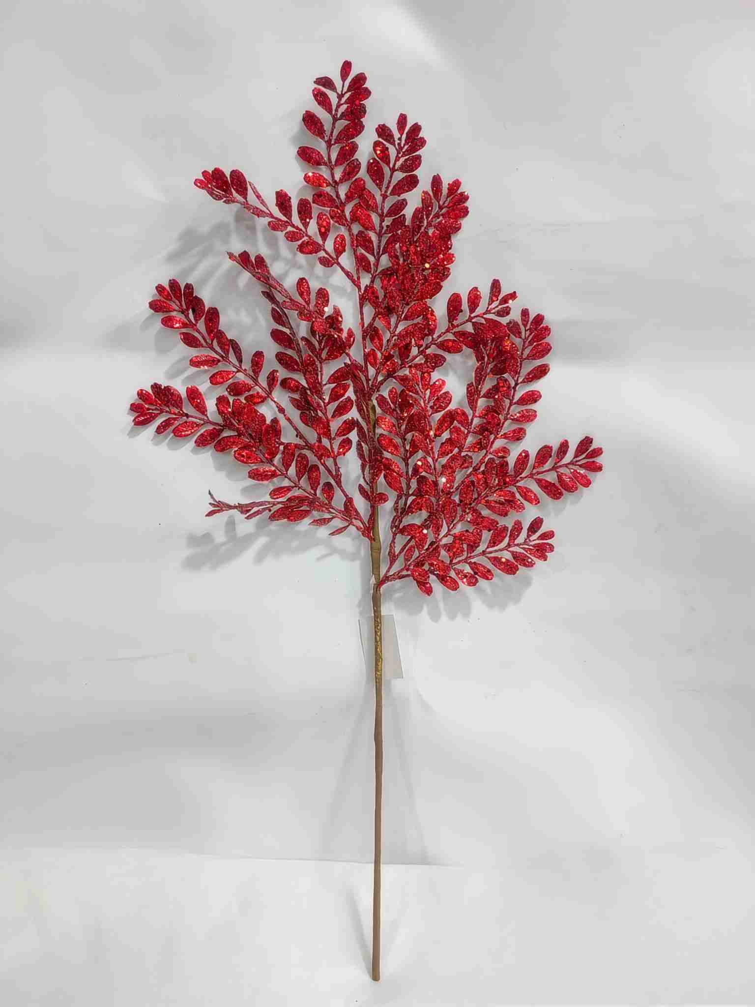 A single red leafy branch with a shiny, glittery appearance stands out against a plain white background.