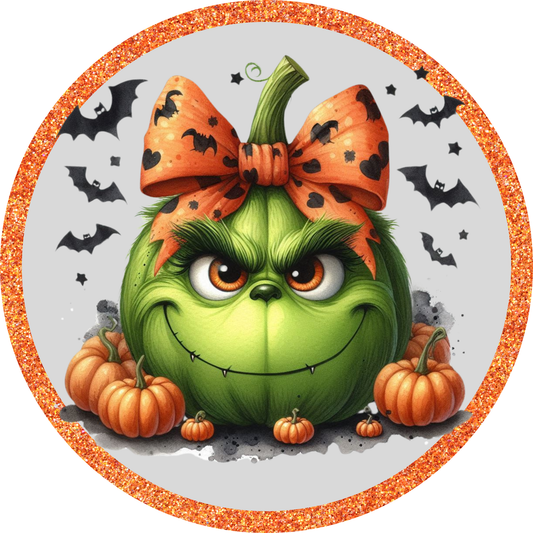 A grumpy-looking green pumpkin with a bow and a pair of orange bats surrounding it, set against a glittery orange border.