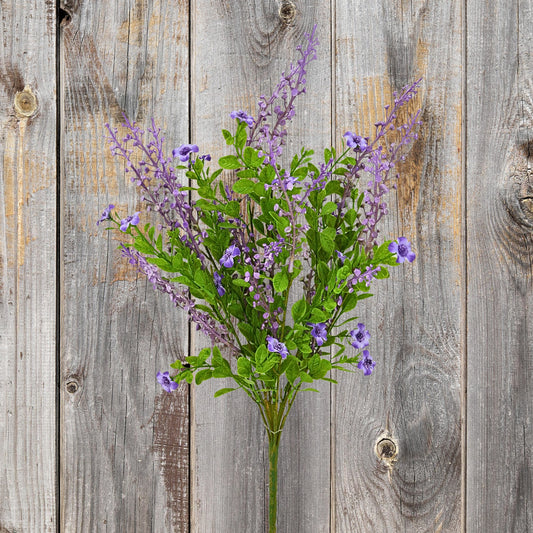 A bouquet of purple flowers with green leaves is displayed against a weathered wooden background.