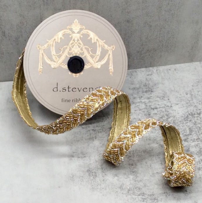 A gold-colored ribbon with a decorative pattern is displayed next to a round, white label with gold lettering and an ornate design.