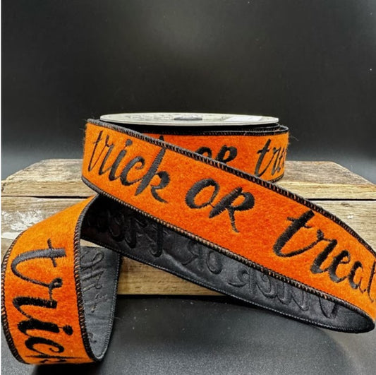 A spool of orange and black striped ribbon with the text "trick or treat" printed on it, placed on a wooden surface.