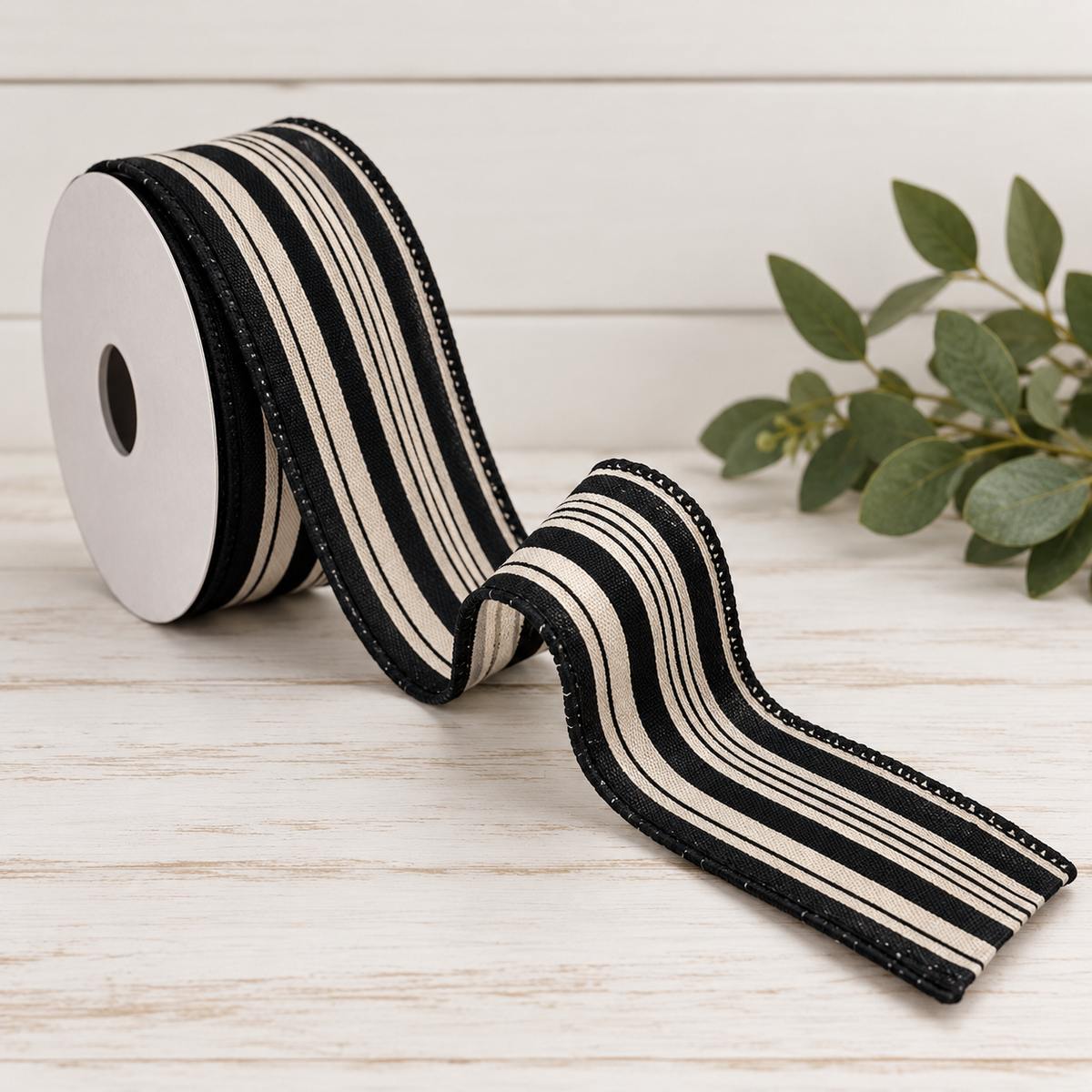 A roll of black and white striped ribbon is placed on a white wooden surface, with a green plant in the background.