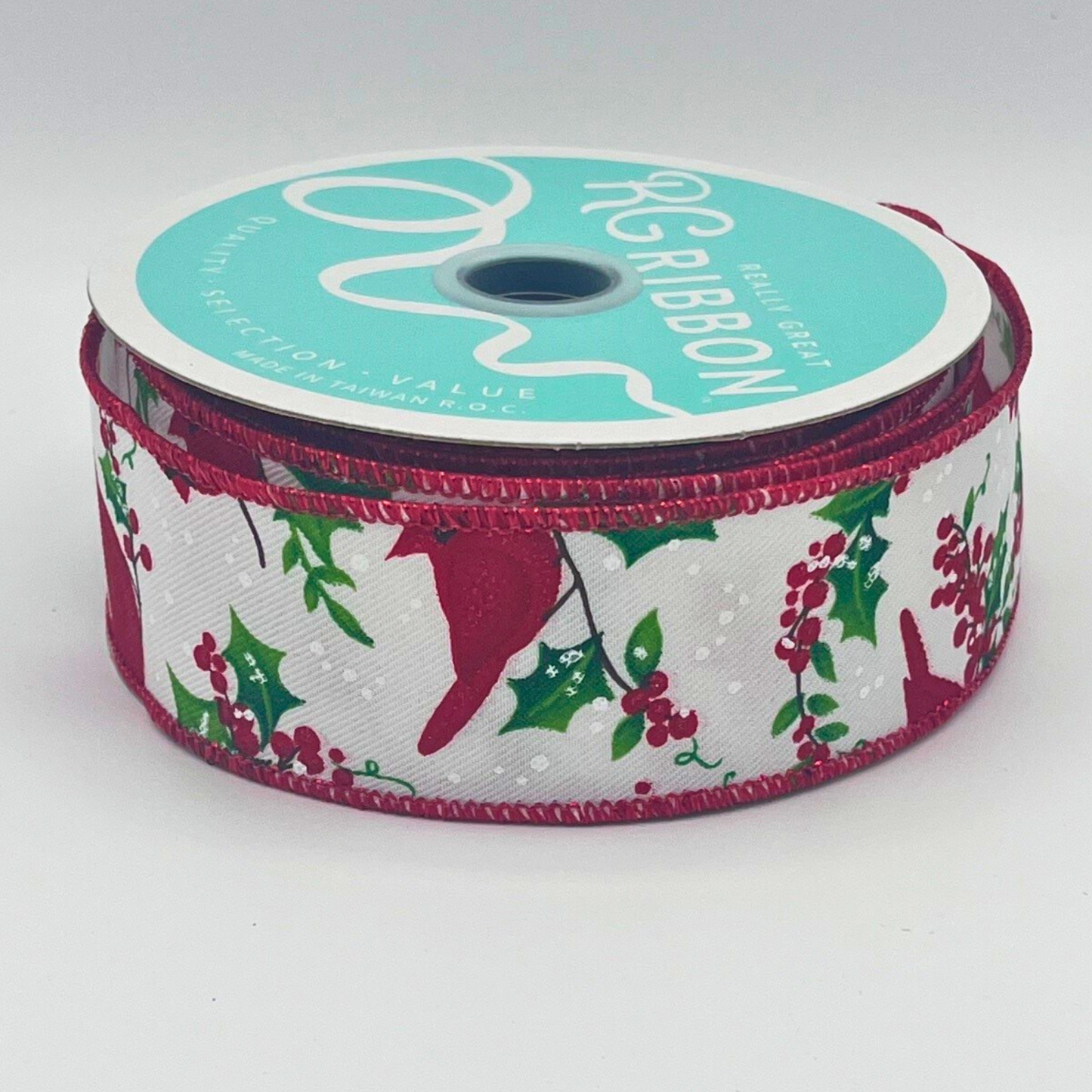 A spool of turquoise ribbon with a red and white pattern of holly and berries, placed on a white surface.