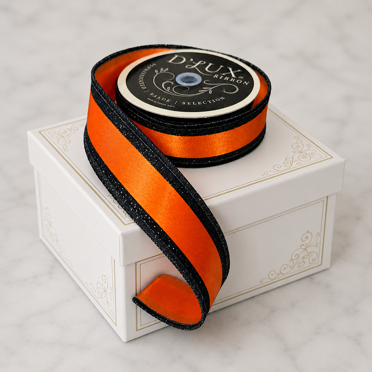 A roll of black and orange ribbon is placed on top of a white box with a gold border.