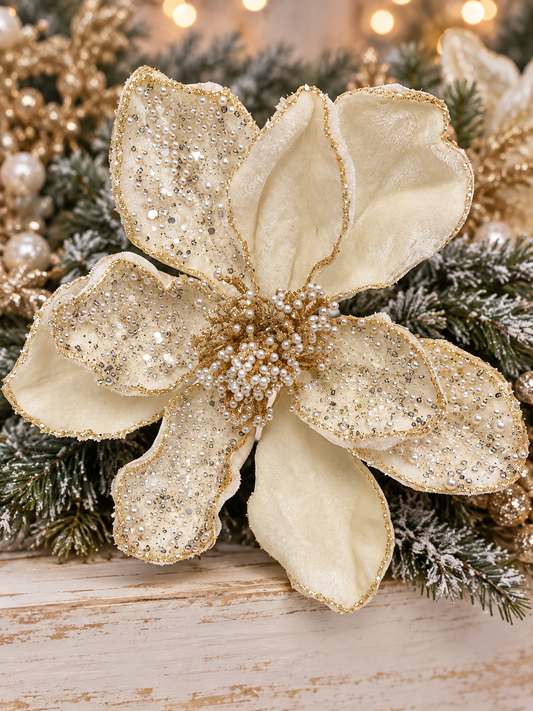 A close-up of a large, ornate gold and white flower with sparkling embellishments, surrounded by greenery and twinkling lights.