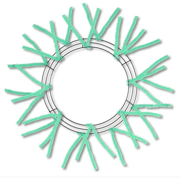 A circular wreath made of green pipe cleaners, with the pipe cleaners arranged in a radial pattern around the center of the wreath.