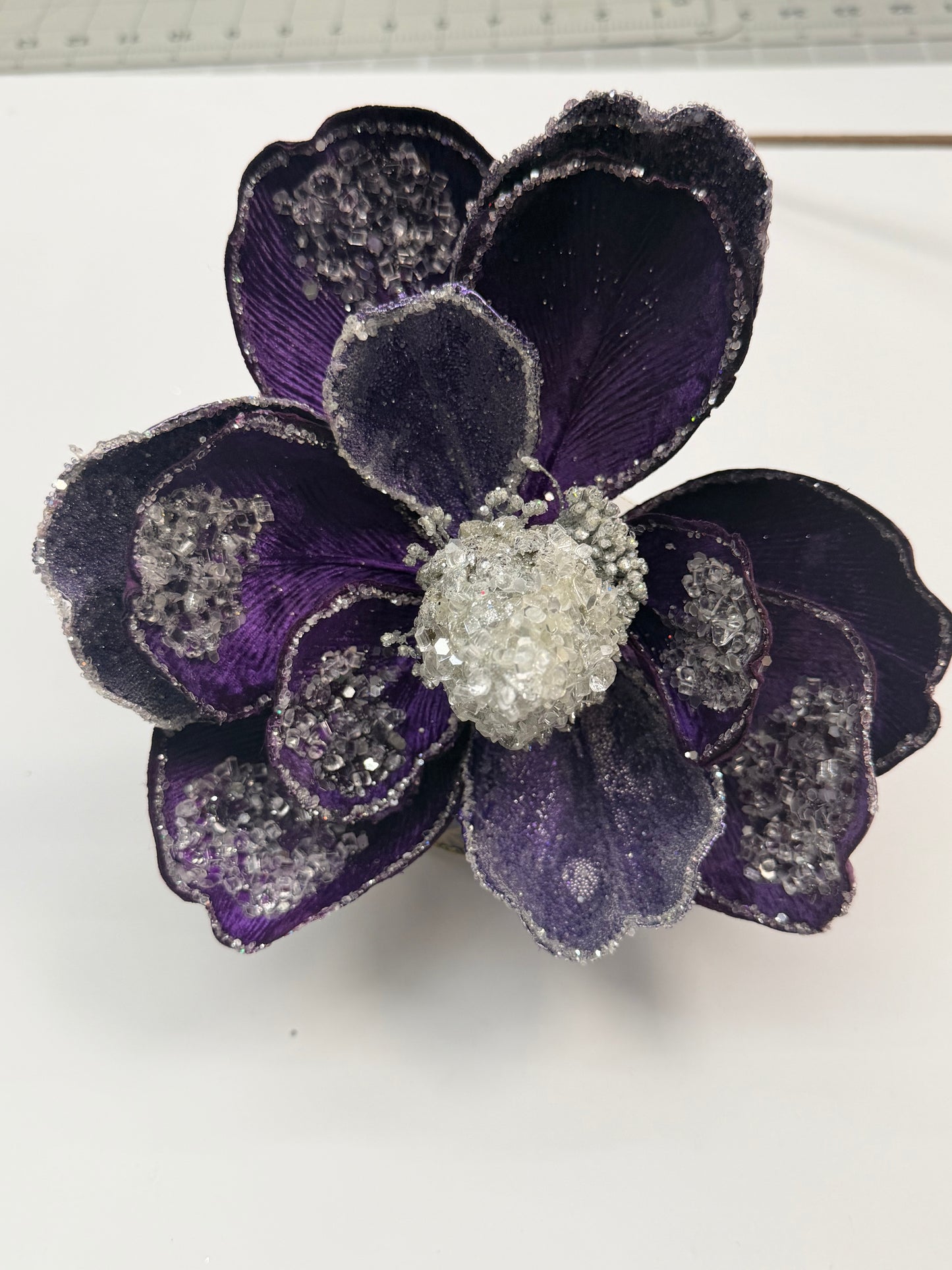 A close-up view of a purple flower with a white center, adorned with sparkling crystals or jewels.