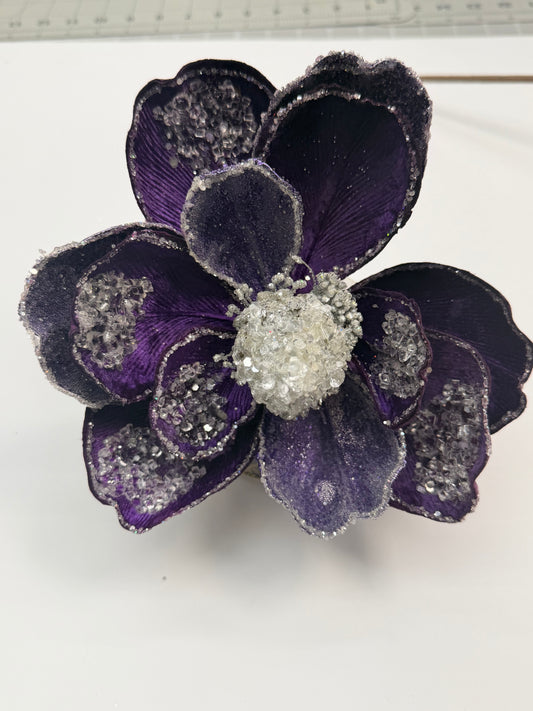 A close-up view of a purple flower with a white center, adorned with sparkling crystals or jewels.