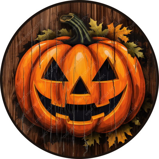 A large, orange jack-o-lantern with a carved face and a green stem is displayed on a wooden surface, surrounded by autumn leaves.