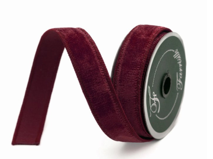 A burgundy velvet ribbon is coiled and resting on a white background.