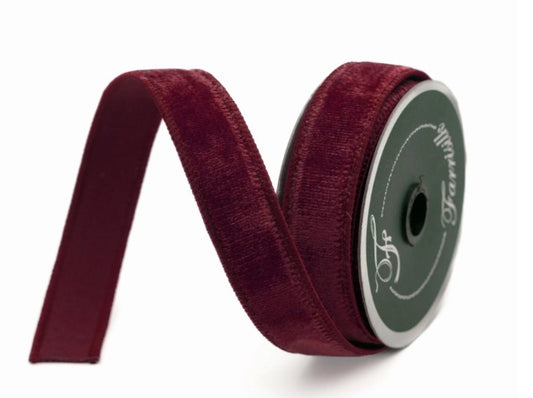 A burgundy velvet ribbon is coiled and resting on a white background.