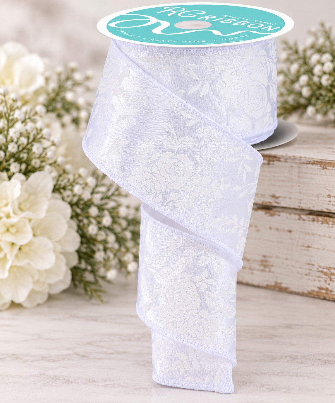 A white floral lace ribbon is displayed on a wooden surface, with white flowers in the background.