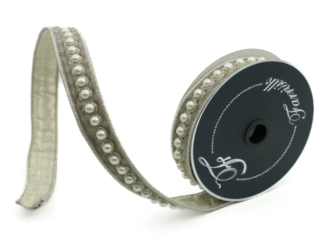 A silver-colored ribbon with a decorative pattern of small white pearls on it, lying on a white background.