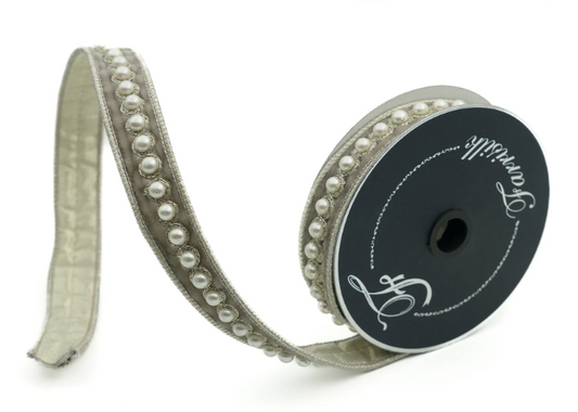 A silver-colored ribbon with a decorative pattern of small white pearls on it, lying on a white background.